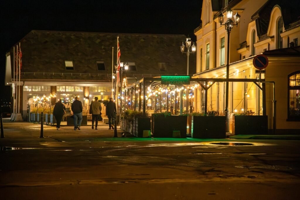 Vibrant night view of Ålesund's downtown with illuminated street restaurant and five people walking.
